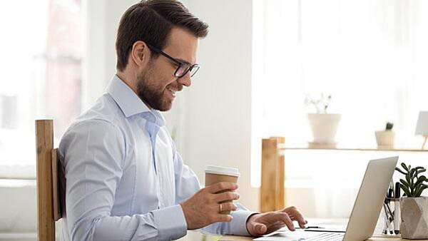 Caucasian business man holding coffee whilst looknig at laptop