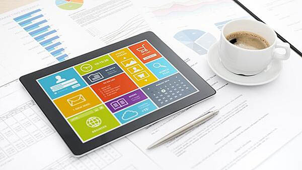Tablet sitting on top of charts with cup of coffee next to it