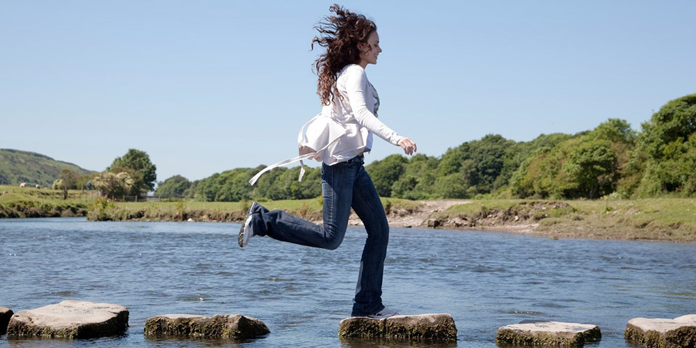 Female jumping across stones in water