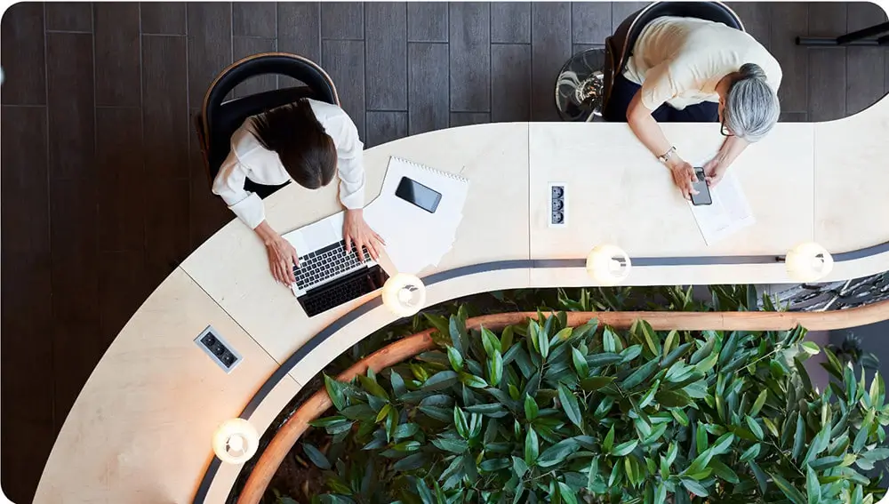 Top down view of two workers using laptop and phone at modern curved desk