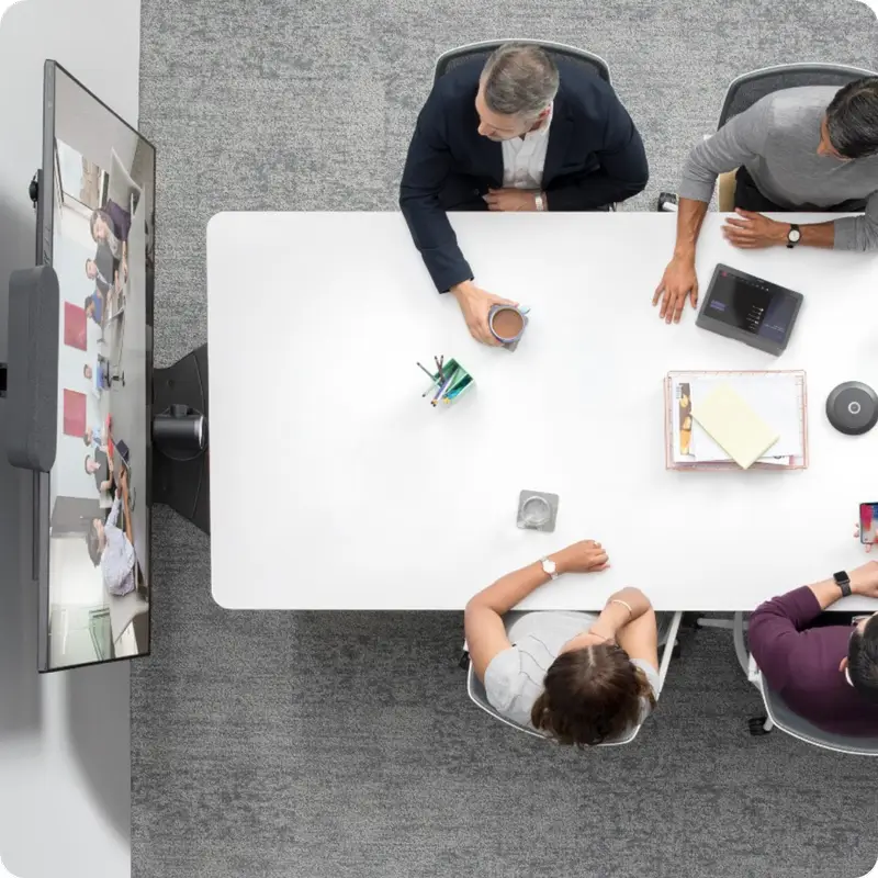 Top view of 4 people in a meeting with other team members virtually, presumably via hybrid workplace